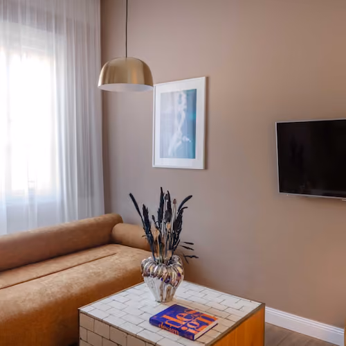 Modern living room with a brown couch, coffee table, wall art, hanging lamp, and TV on tan wall.