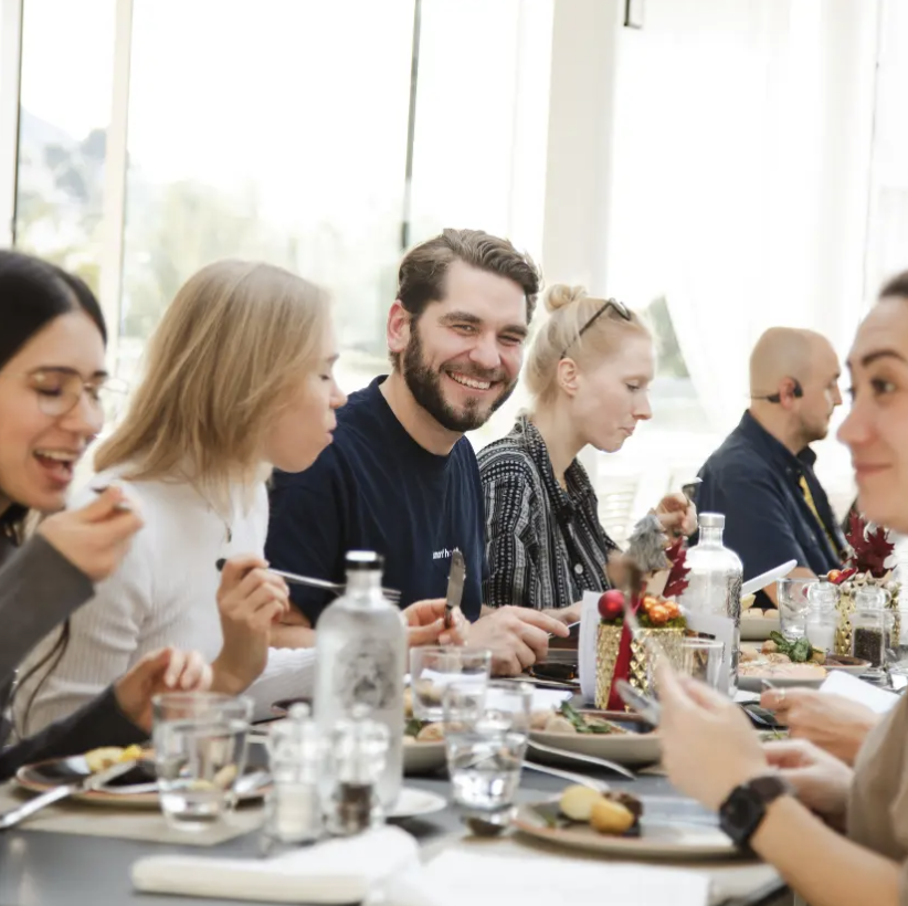 Group of five people sitting at a table indoors eating and smiling during a meal.