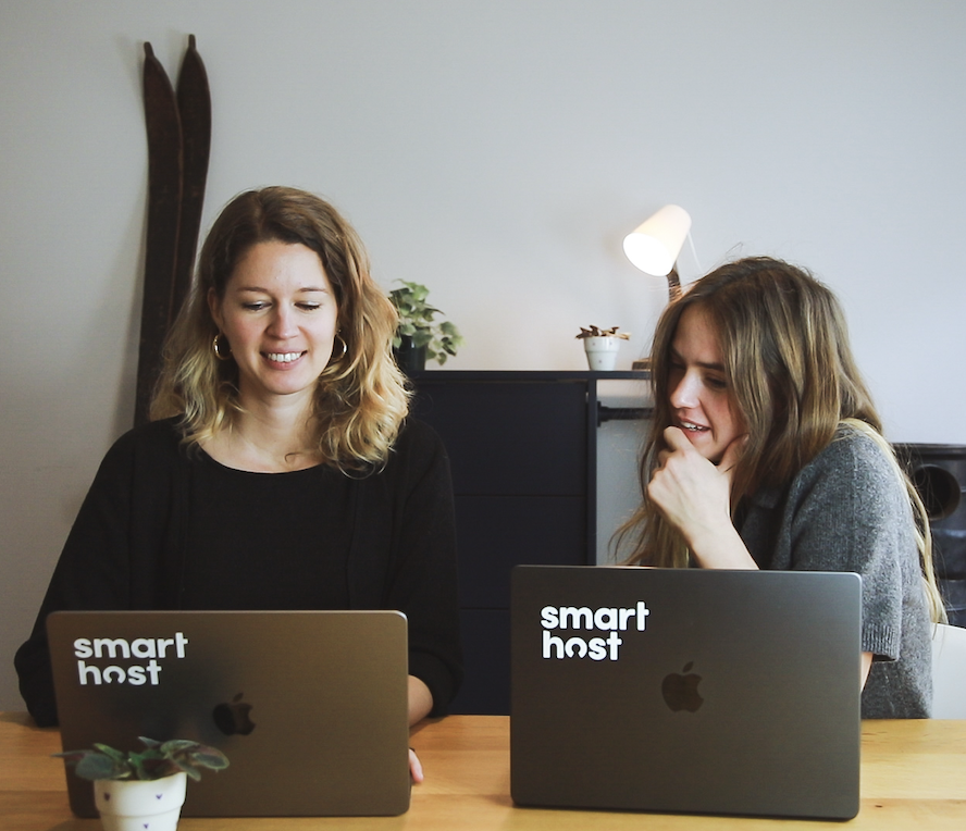 Two women work on laptops with Smart Host stickers at a wooden table in a modern office.