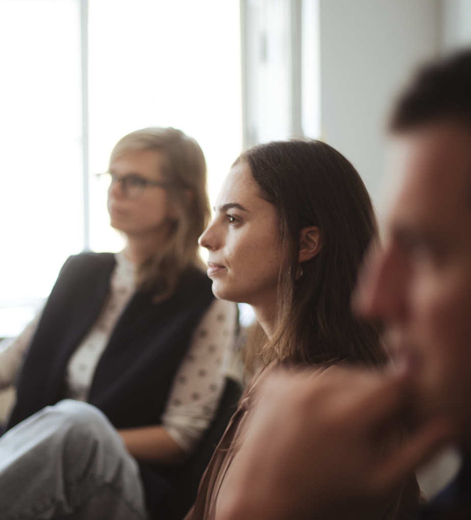 Three people sitting indoors, with the focus on a woman in the middle listening attentively.