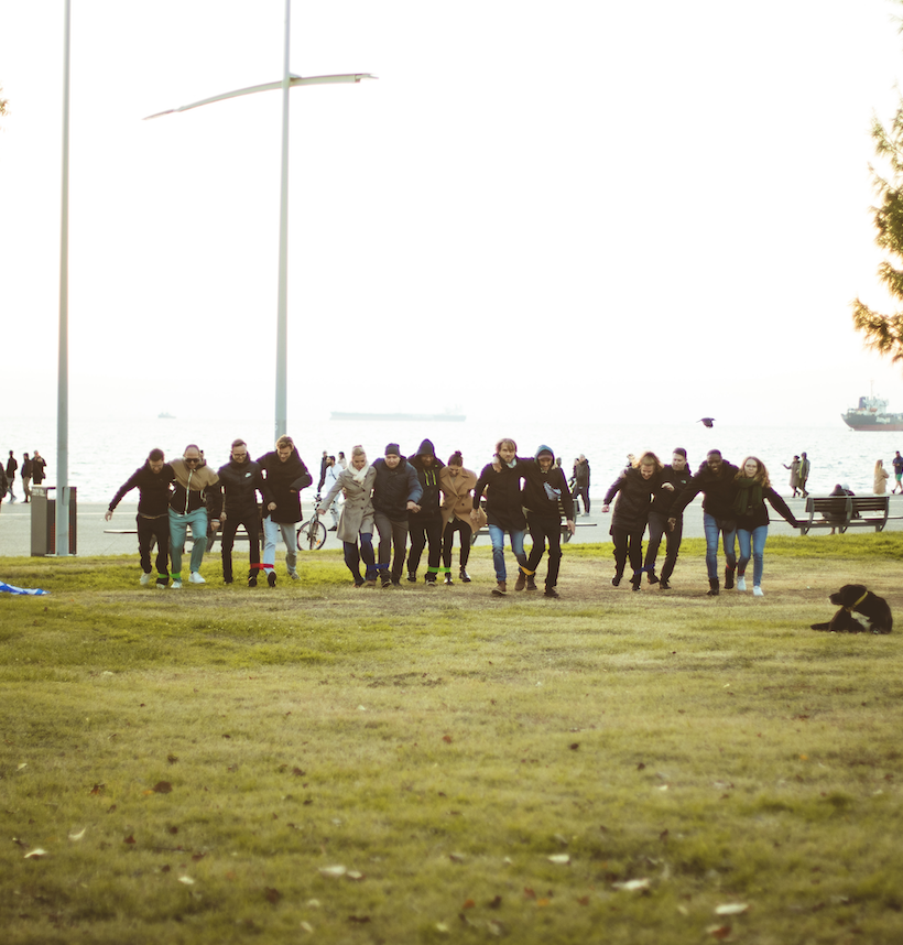 Group of people racing or running outdoors near a waterfront on grass with ships in the background.