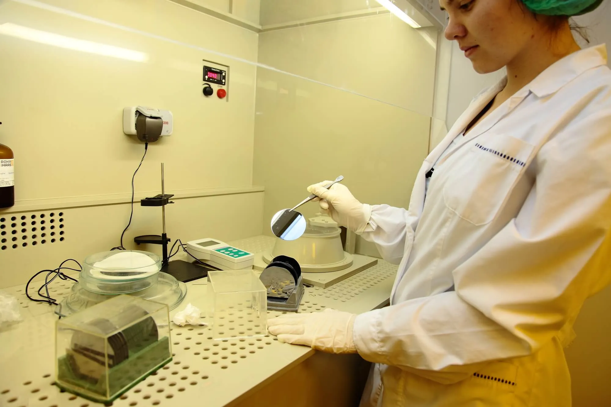 A woman in a silicon manufacturing lab holding a wafer and looking at it