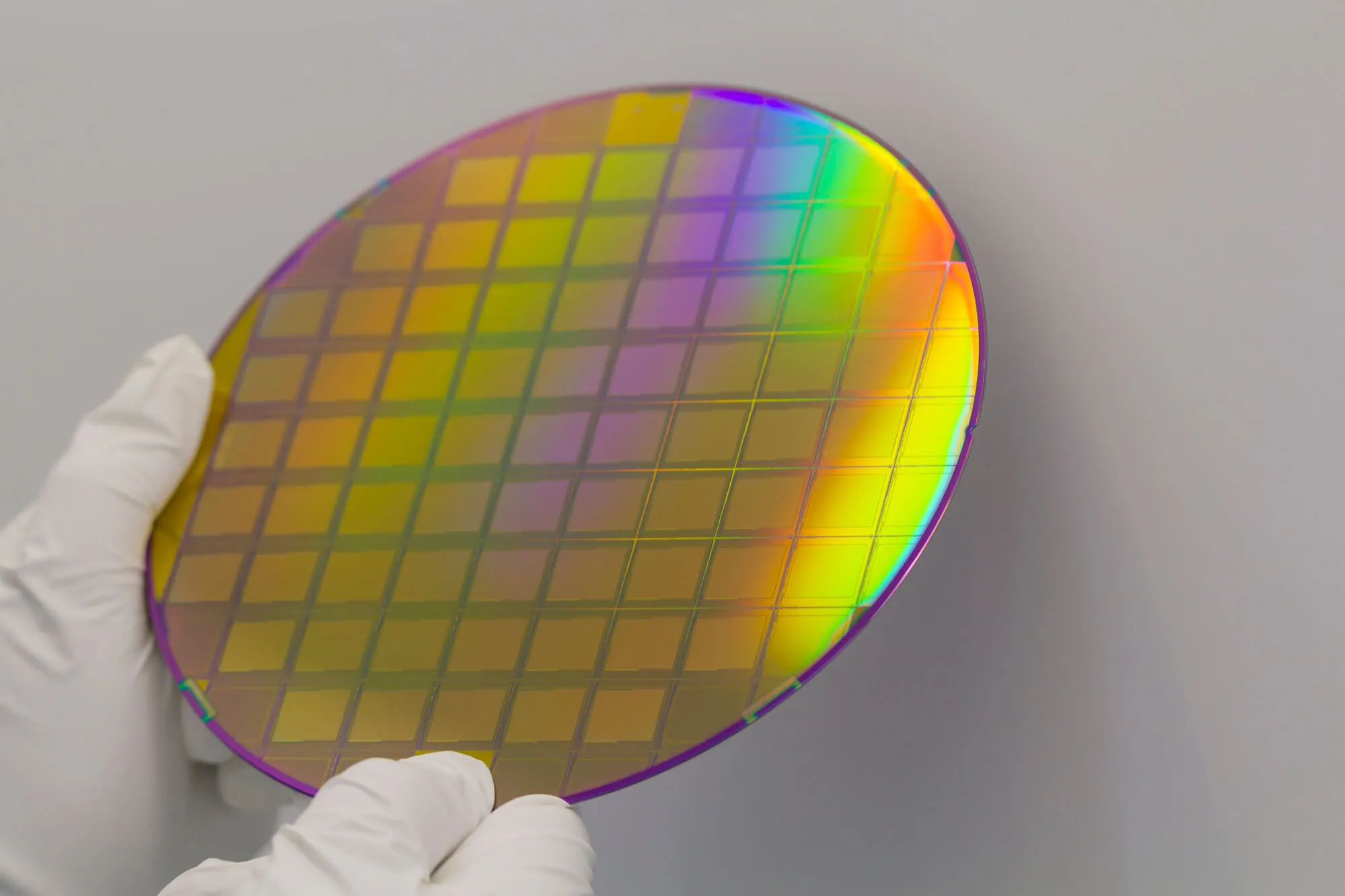 Close up of a silicon wafer being held by someone with white gloves