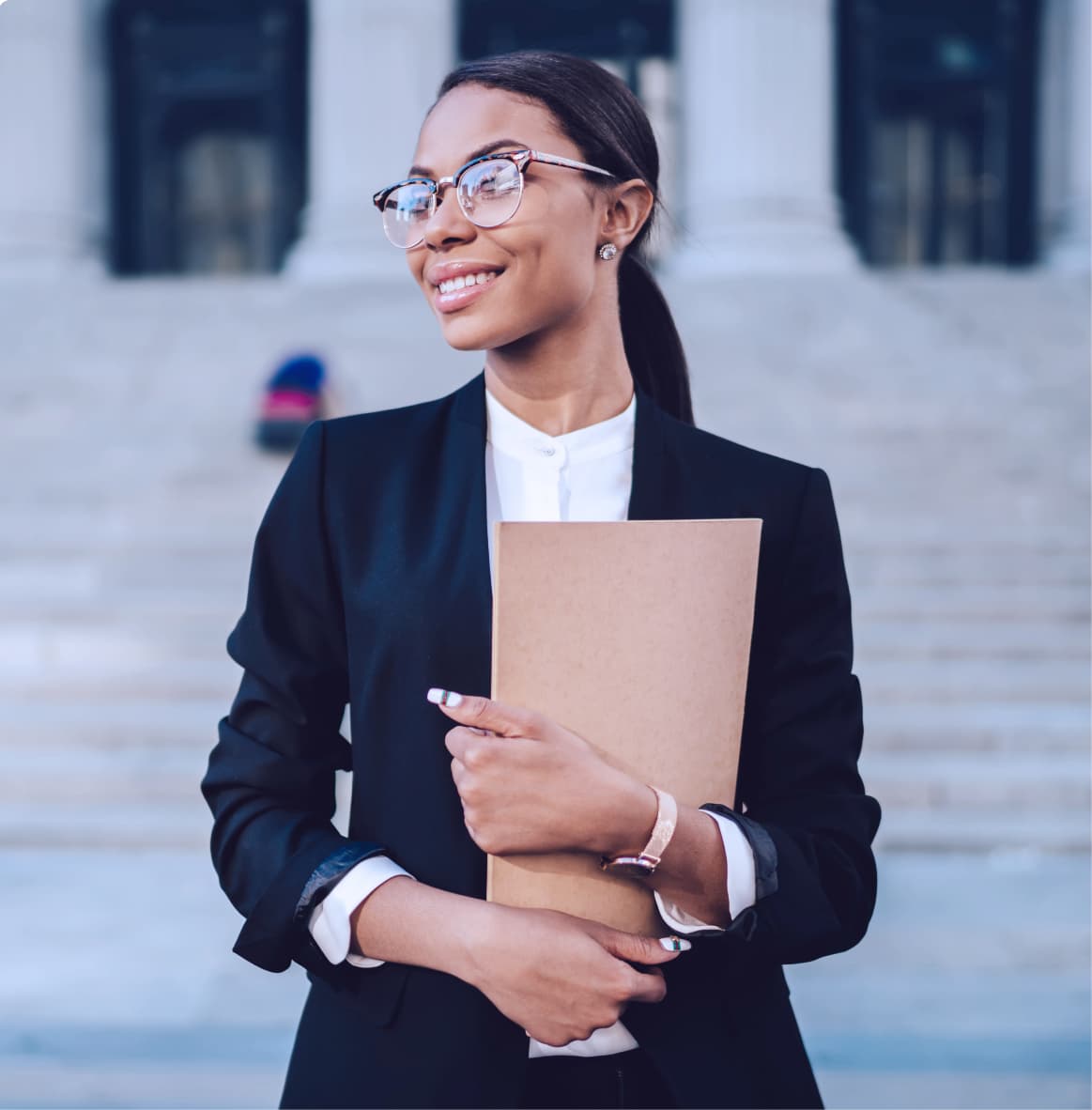 A confident young woman in a black blazer and glasses smiles while standing in front of a courthouse. She holds a large kraft folder and looks off into the distance, conveying professionalism and ambition.