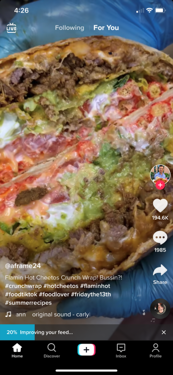Home page of TikTok after first signing up. It shows a video of a burger, the username and profile picture of the creator, the caption of the video, the Like button, the Comment button, the Share button, and a Sound button.