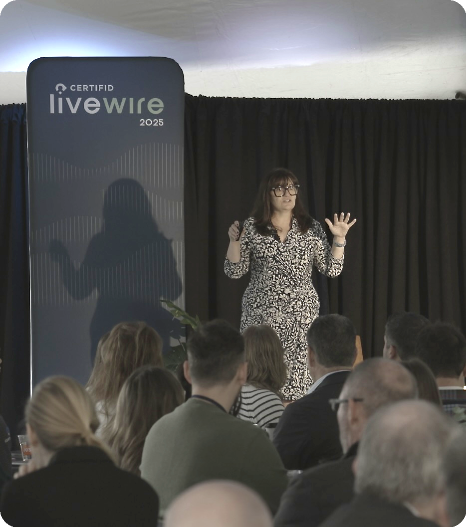 Erin West speaks on stage at a LiveWire, wearing a patterned dress. A banner behind her reads "CERTIFID Livewire 2025." 