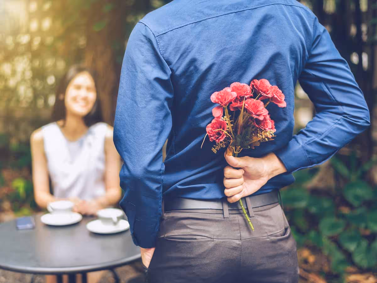 Man hiding flowers behind his back Woman sitting in the background