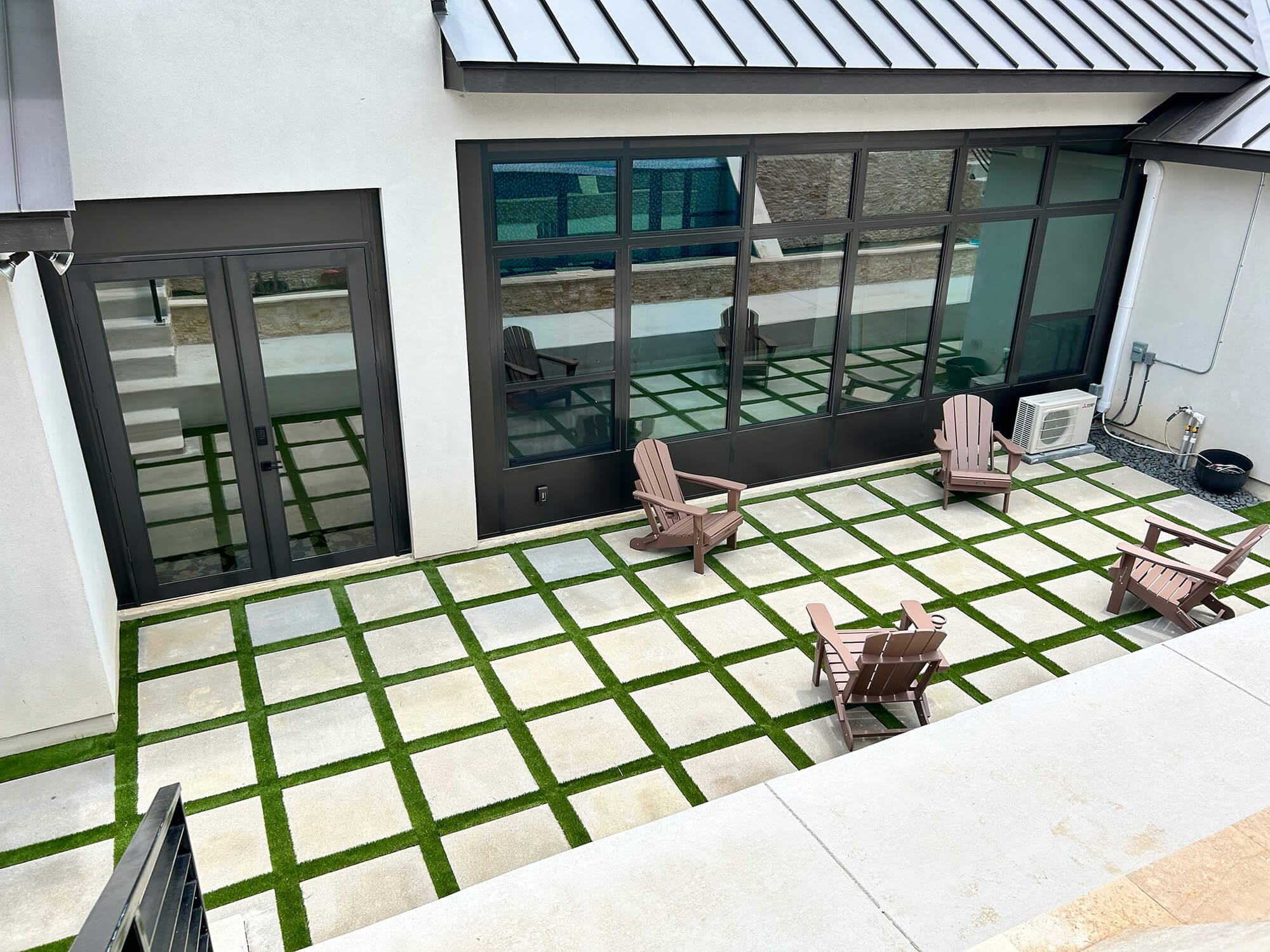 Modern patio with grid stone and grass design, wooden chairs.