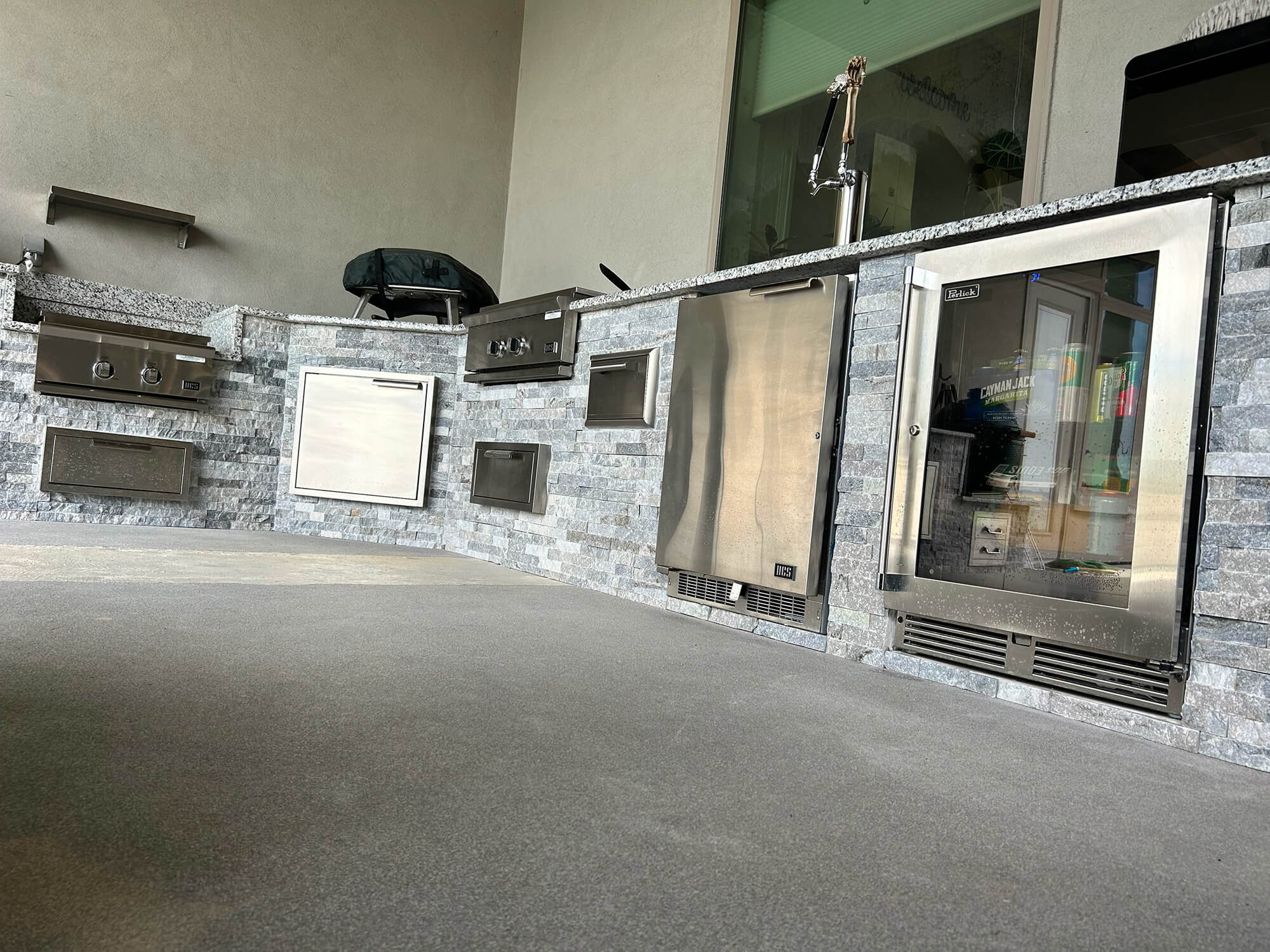 Outdoor kitchen with grill, fridge, and stone finish.