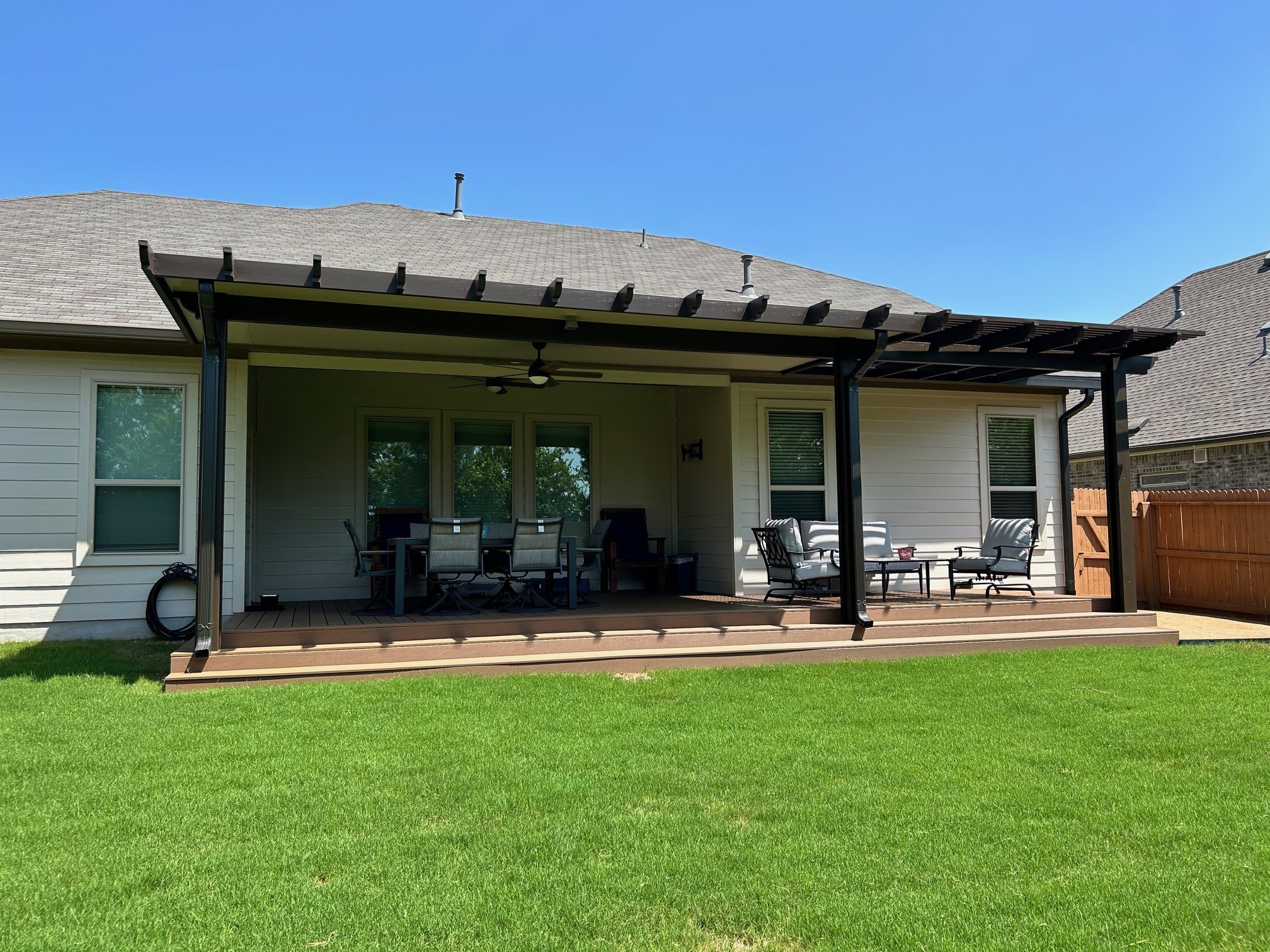 Wooden patio cover with pergola over a backyard patio with outdoor furniture, sunny day, clear blue sky.