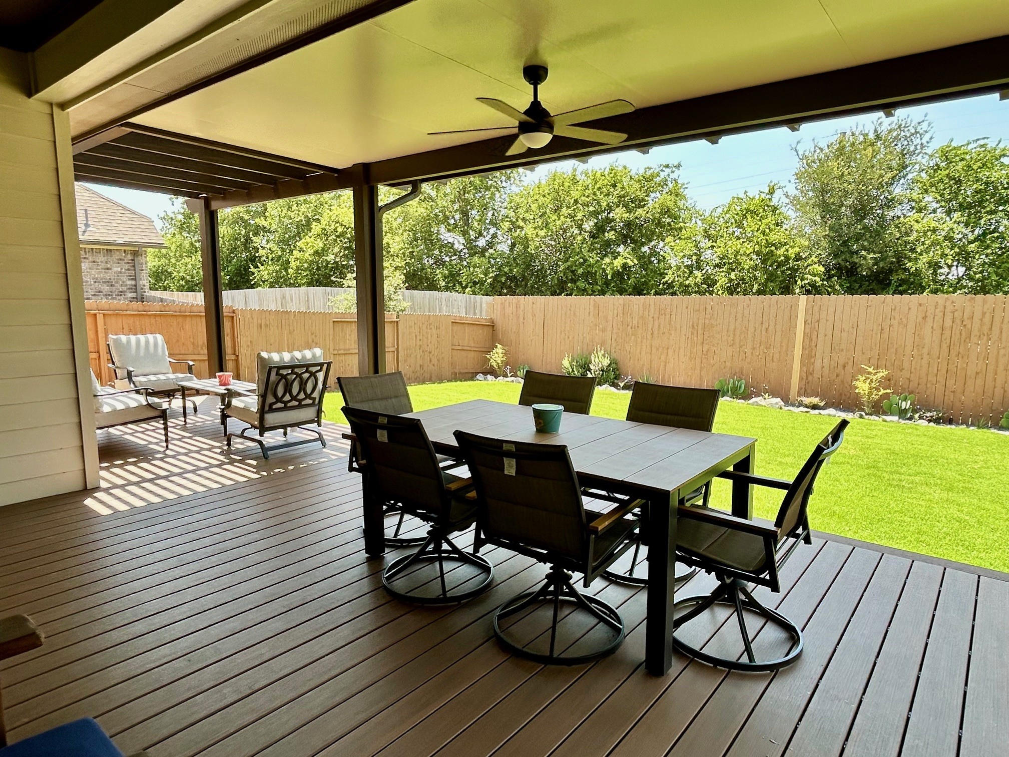 Wooden patio cover with pergola over a backyard patio with outdoor furniture, sunny day, clear blue sky.