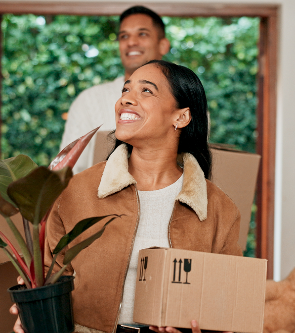 Happy couple moving into their new home carrying boxes and plants