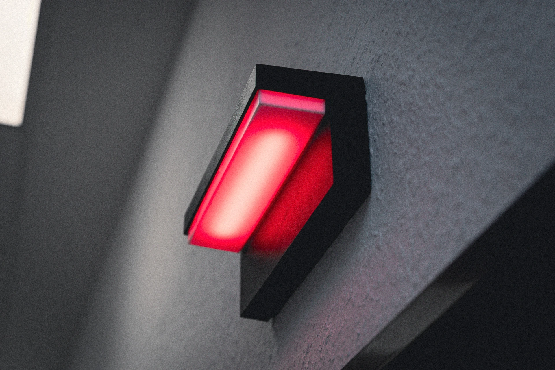 Wandlampe mit roter Leuchtfläche an grauer raue Wand befestigt.