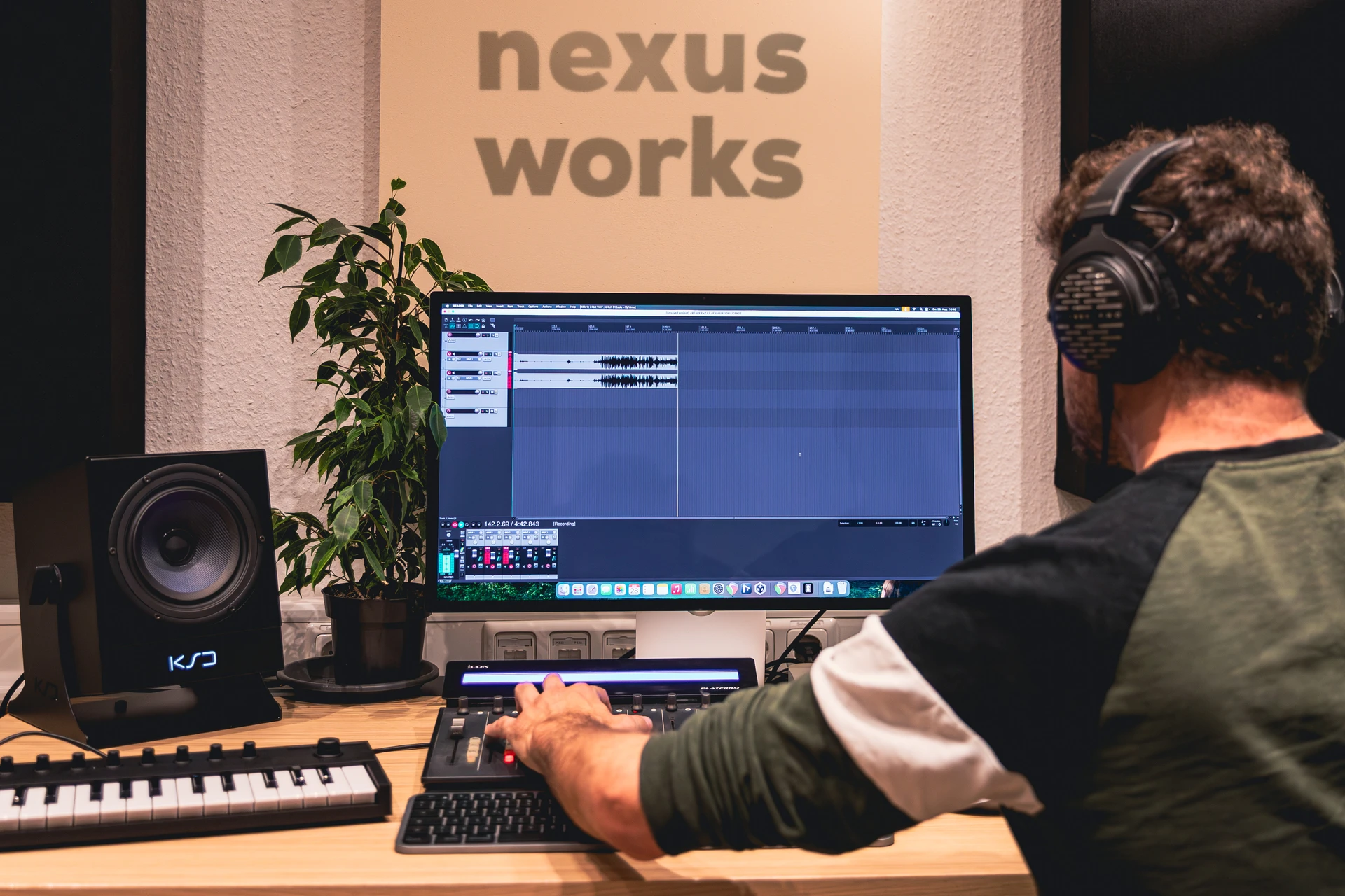 Person mit Kopfhörern arbeitet an einem Audiobearbeitungsprogramm auf einem Computer im Studio.