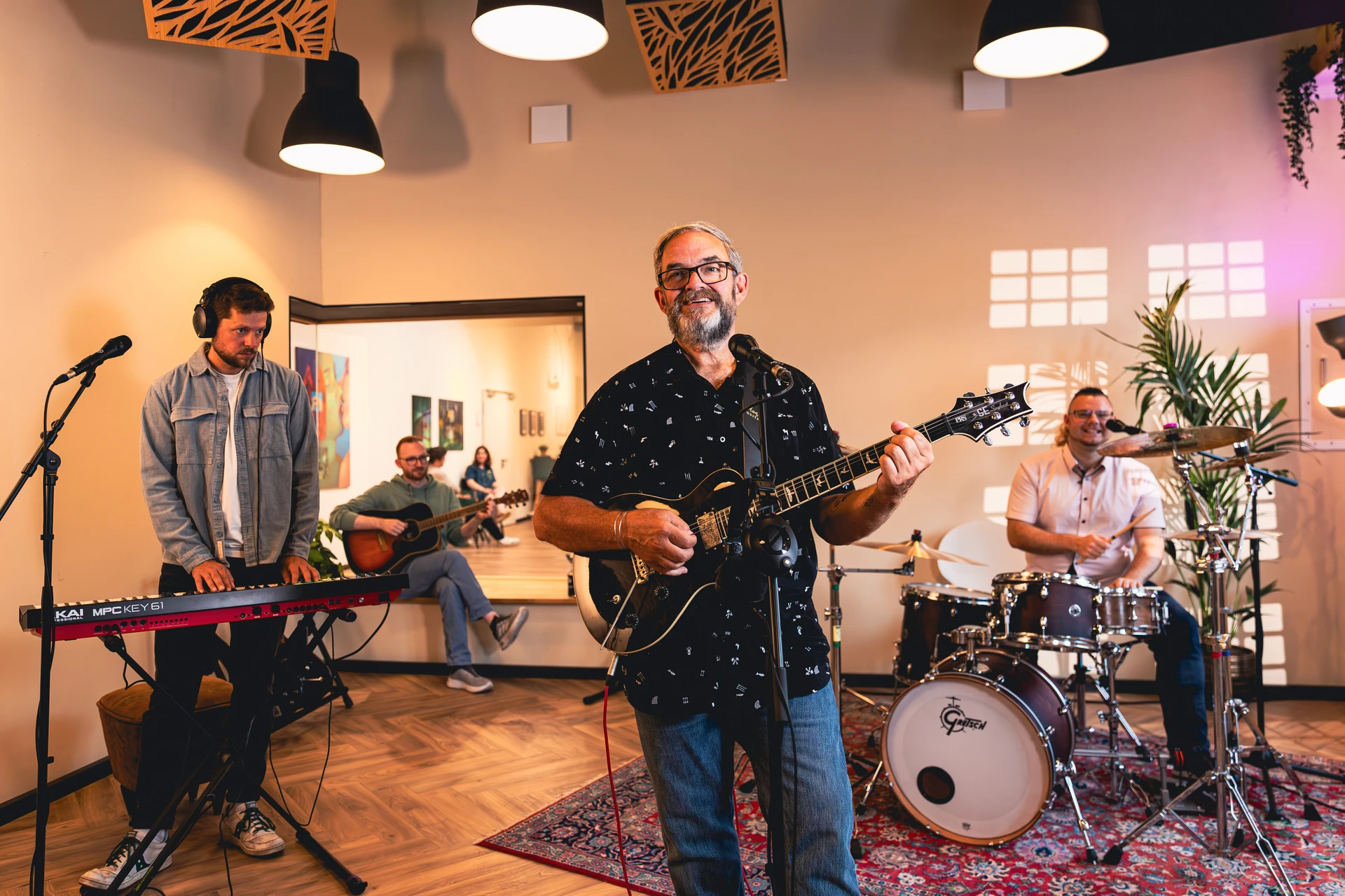 Vierköpfige Band im Aufnahmeraum, mit einem Gitarristen vorne, Keyboarder links, Schlagzeuger rechts und einem Gitarristen im Hintergrund.