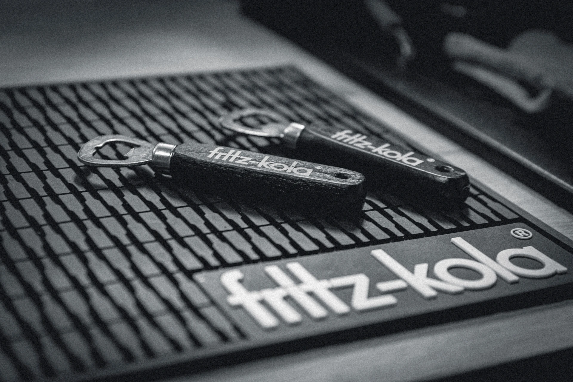 Zwei schwarze Flaschenöffner mit dem Schriftzug 'fritz-kola' liegen auf einer Gummimatte mit demselben Logo.