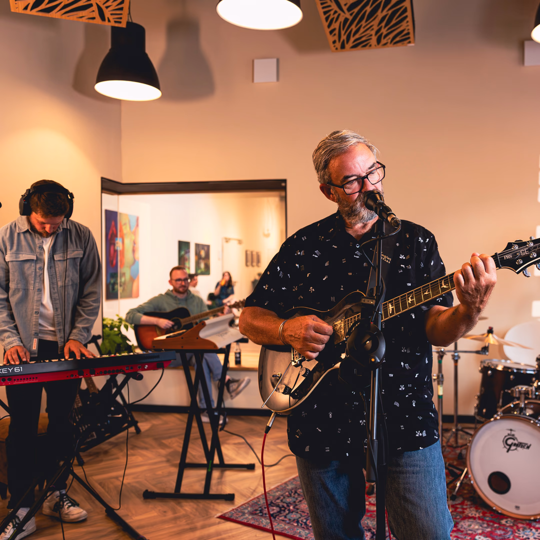 Band spielt Musik in einem Raum mit Schlagzeug, Keyboard und Gitarren, während ein Mann singt.