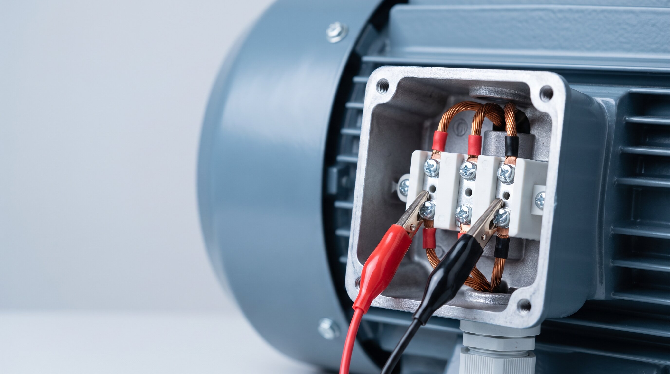 Close-up of test leads clipped to the copper leads on the terminal block of a three-phase industrial electric motor