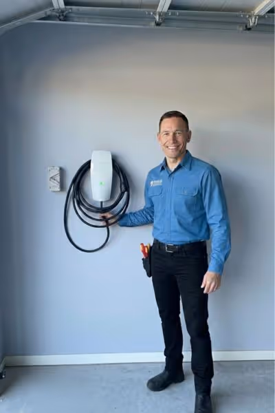 Comma Electrical electrician standing with a recently installed EV charger in a Brisbane home, ready for use