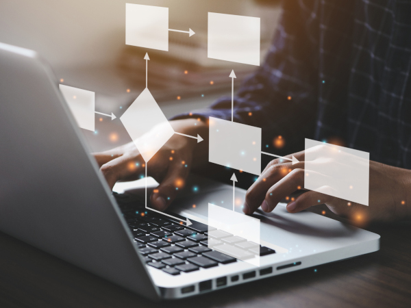Person typing on a laptop keyboard with floating translucent flowchart shapes and arrows overlaid.