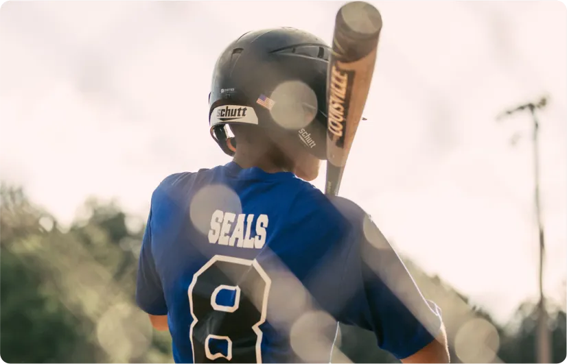 Youth baseball player wearing a blue jersey with number 8 and helmet, preparing to bat with a wooden Louisville Slugger bat.