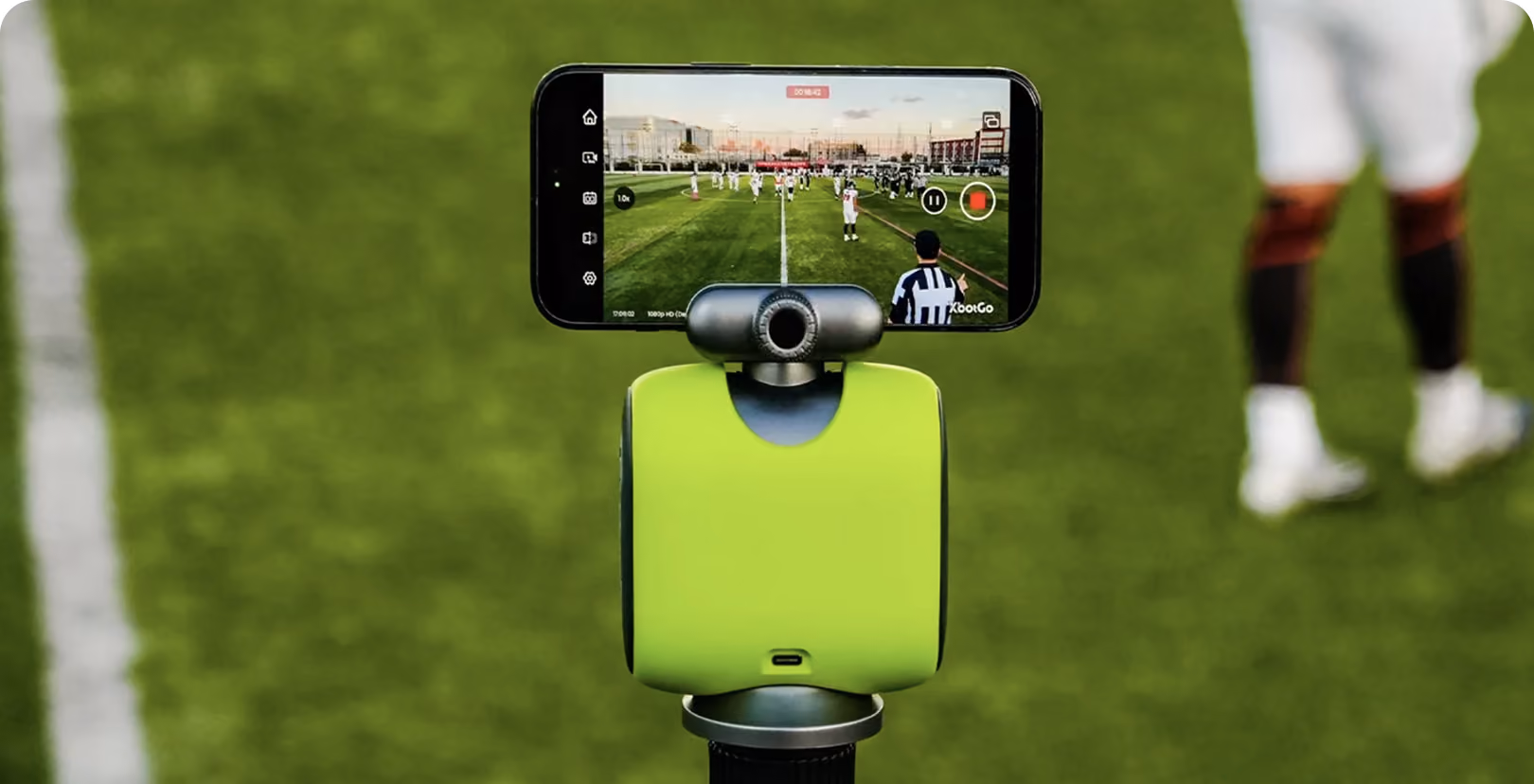 Smartphone on a green device recording an American football game on a grassy field.