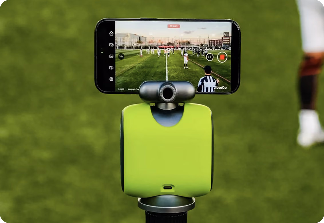 Smartphone on green device live-streaming a football game on a grassy field.