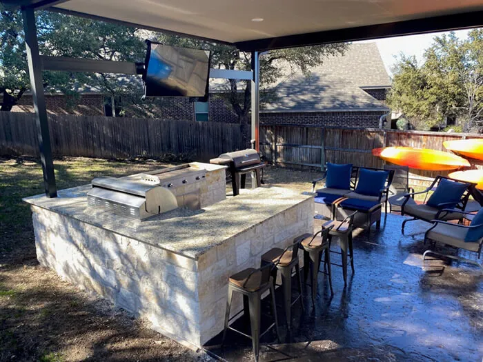 Outdoor kitchen with grill, bar seating, and TVs.