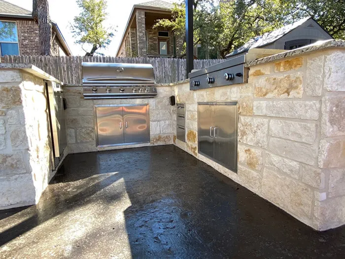 Stone outdoor kitchen with stainless steel appliances in a backyard.