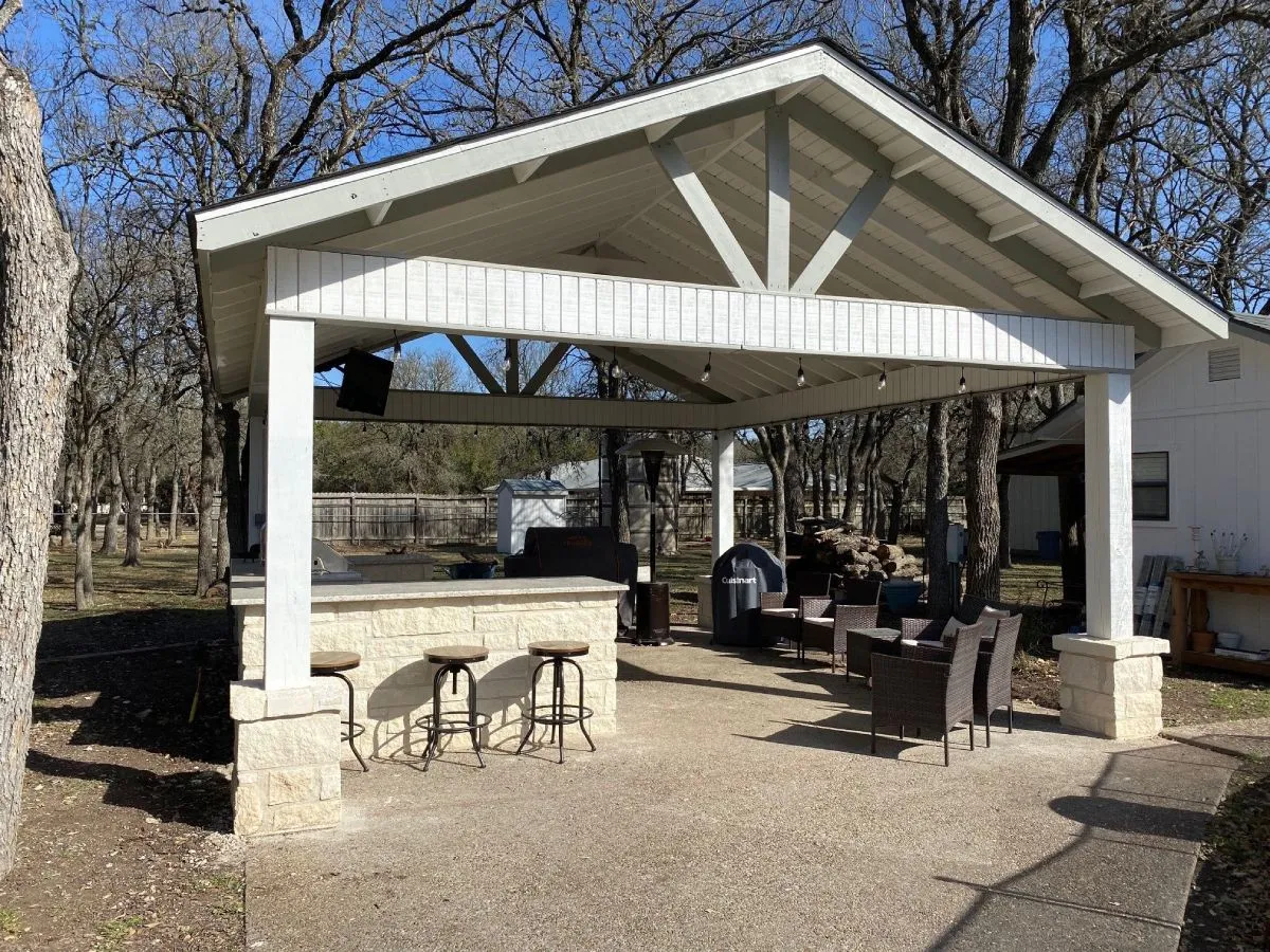 Outdoor kitchen under pergola with bar stools, seating, San Antonio woods.