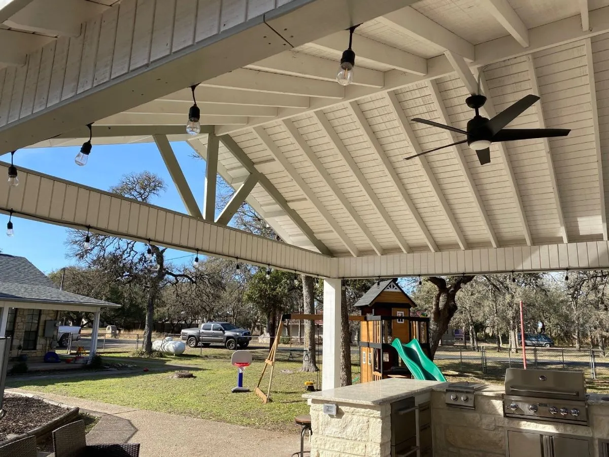 Covered patio with outdoor kitchen and playground in backyard.