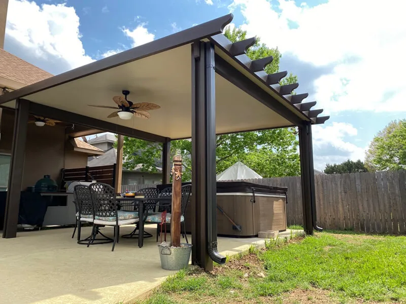 Covered patio with outdoor dining set, fan, and hot tub, surrounded by a wooden fence and greenery.