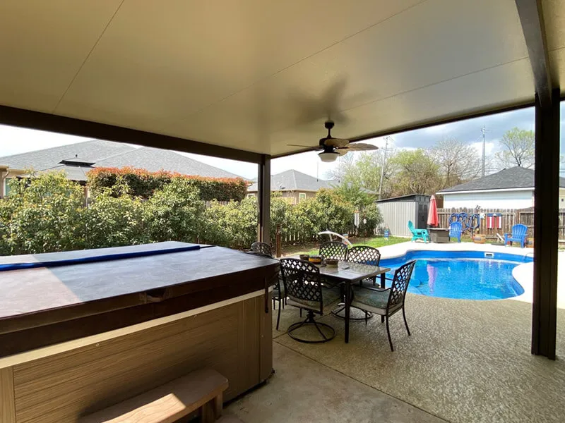 Covered patio with dining set and hot tub overlooking backyard swimming pool and garden.
