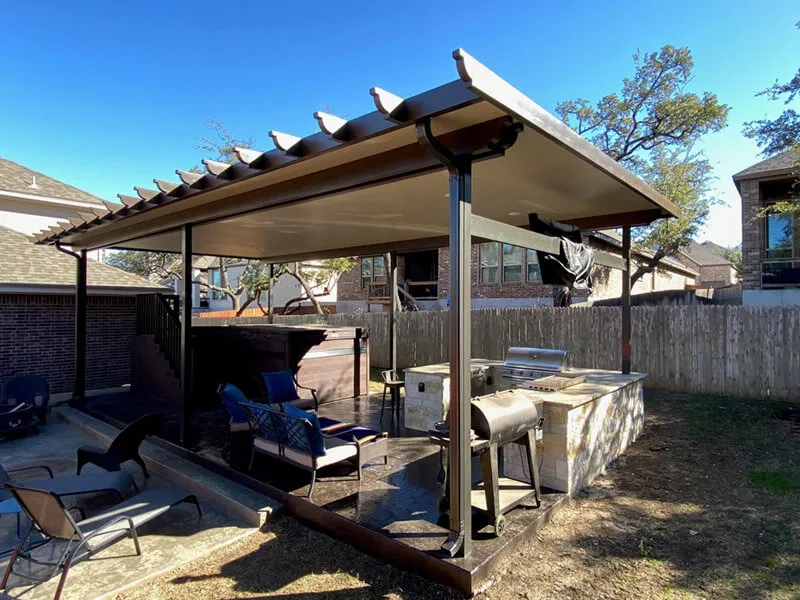 Backyard patio with pergola, outdoor kitchen, and seating under a clear blue sky.