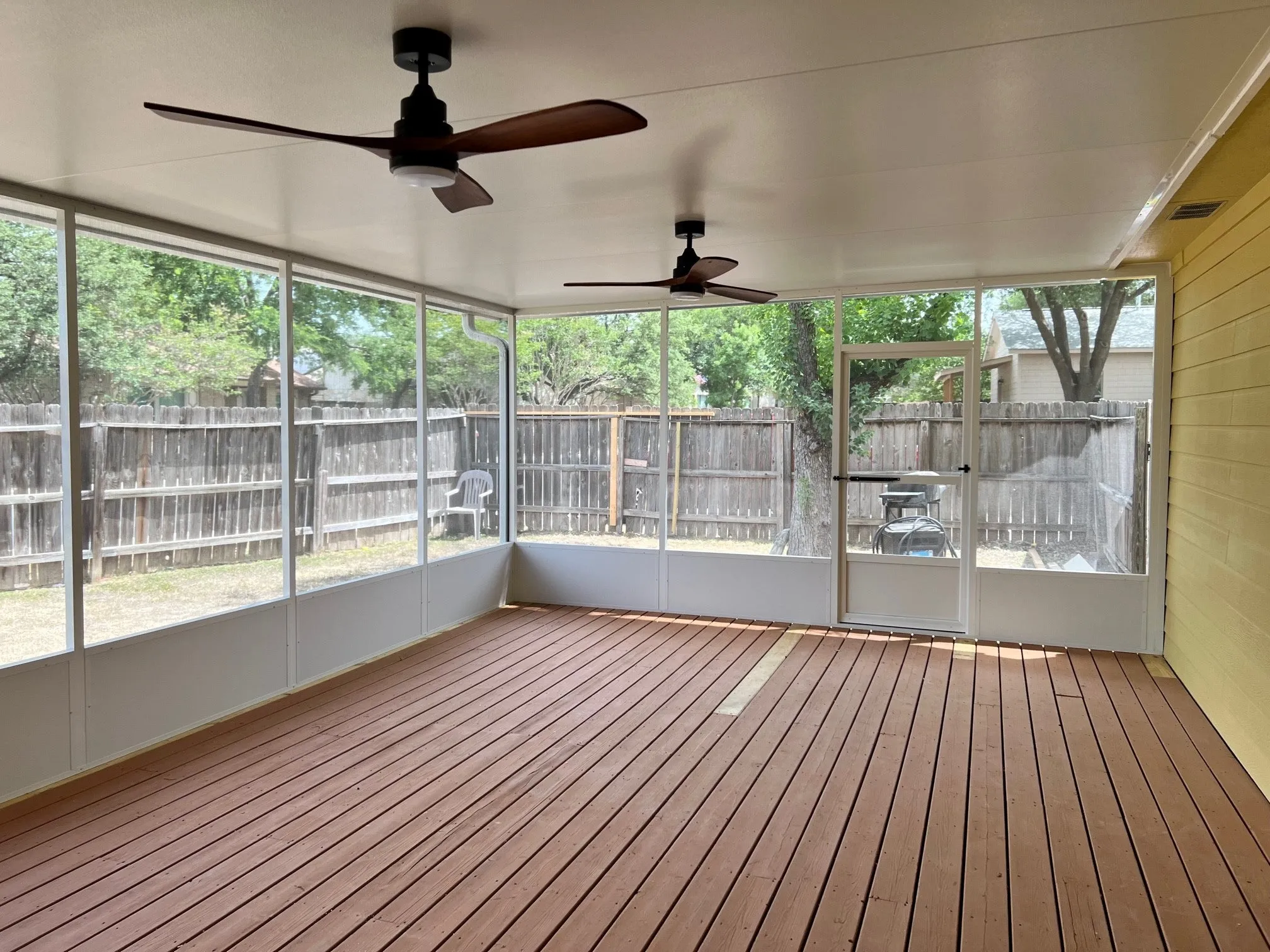 Enclosed patio with wooden floor, ceiling fans, and backyard view.