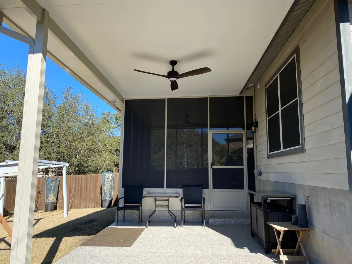 Patio with enclosure, ceiling fan, chairs, table.