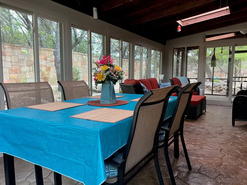 Enclosed patio with blue tablecloth, chairs, and flower centerpiece.
