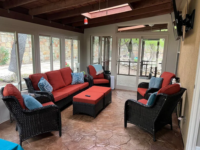 Enclosed patio with wicker furniture, red cushions.