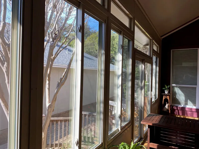 Sunlit patio enclosure with large windows overlooking a yard.