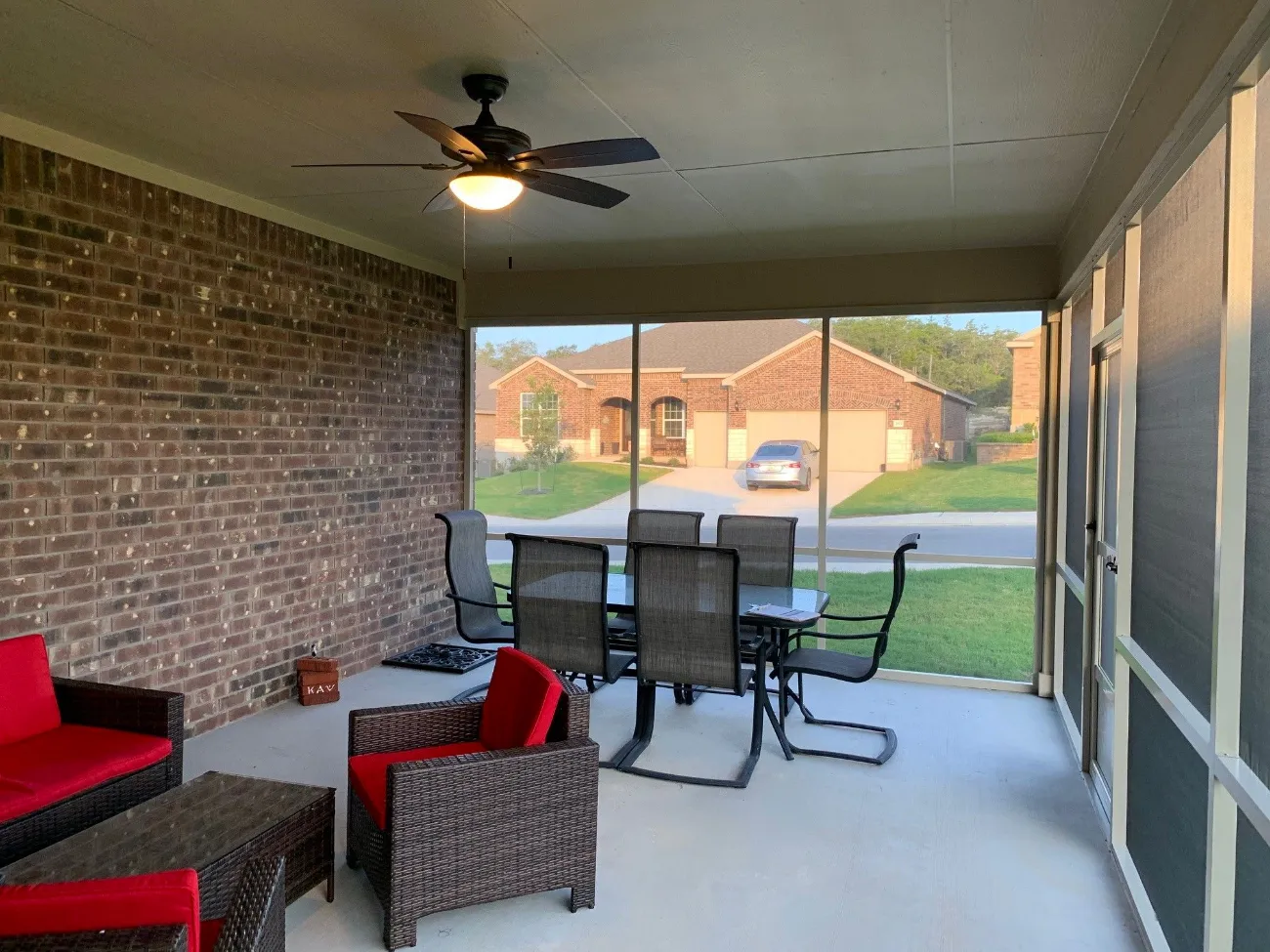 a screened in patio enclosure in san antonio with red pation furniture and a fan