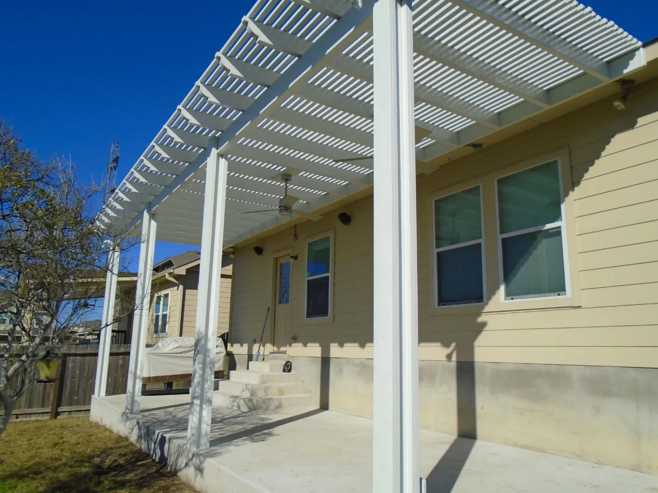 close up view of a white pergola adjacent a home with beige siding