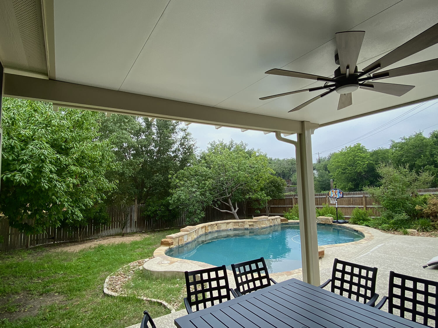Backyard with pool, patio cover, ceiling fan, and table.