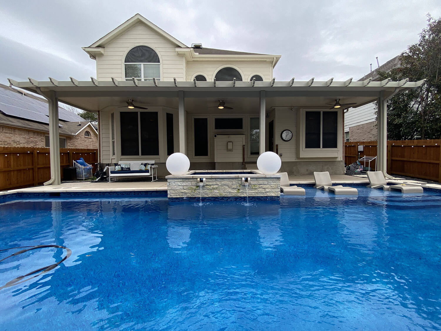 Modern backyard with a swimming pool, lounge chairs, and a patio attached to a two-story house.