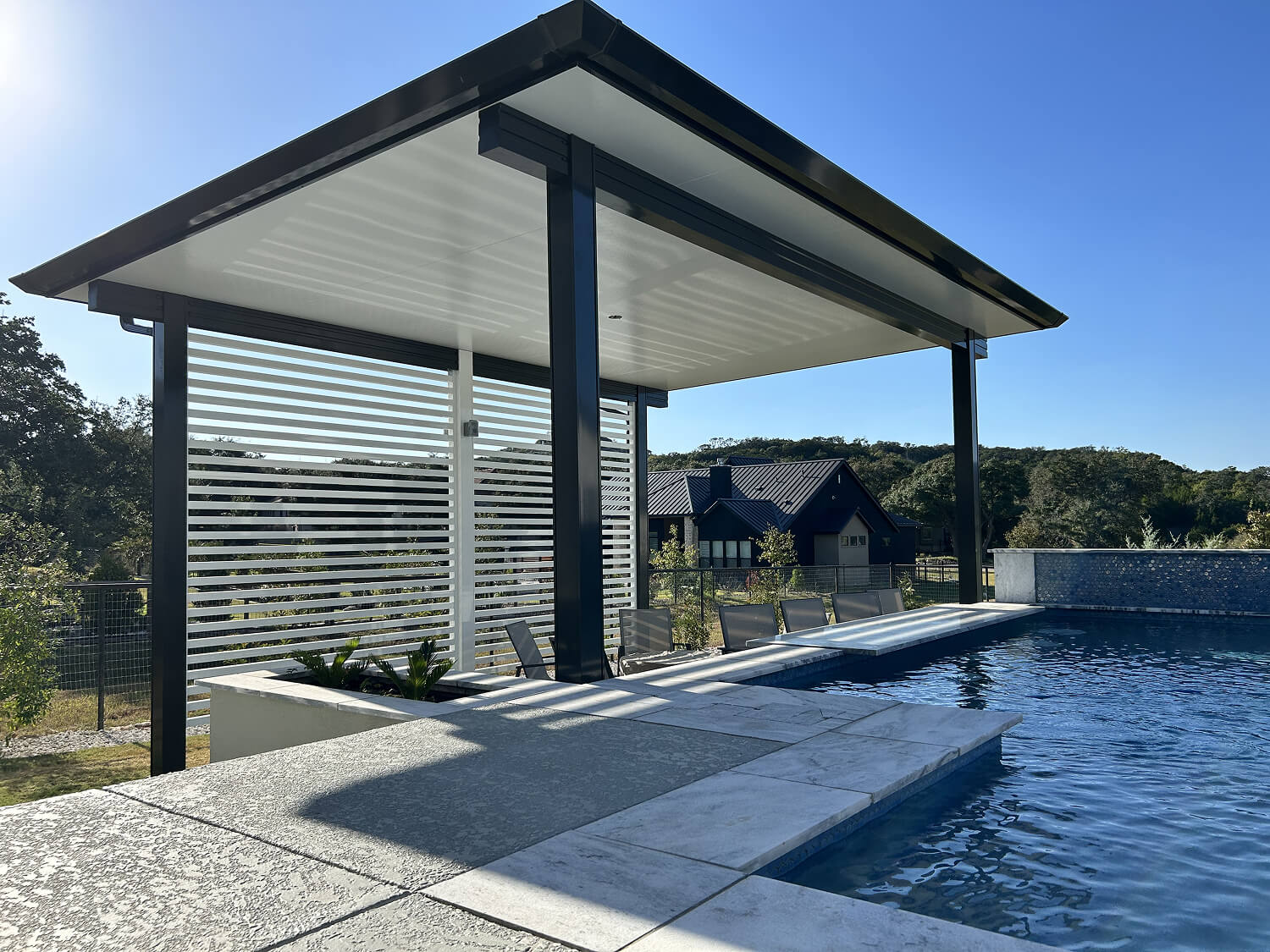 Covered patio with a custom pergola and built-in fireplace, offering a shaded seating area surrounded by mature landscaping.