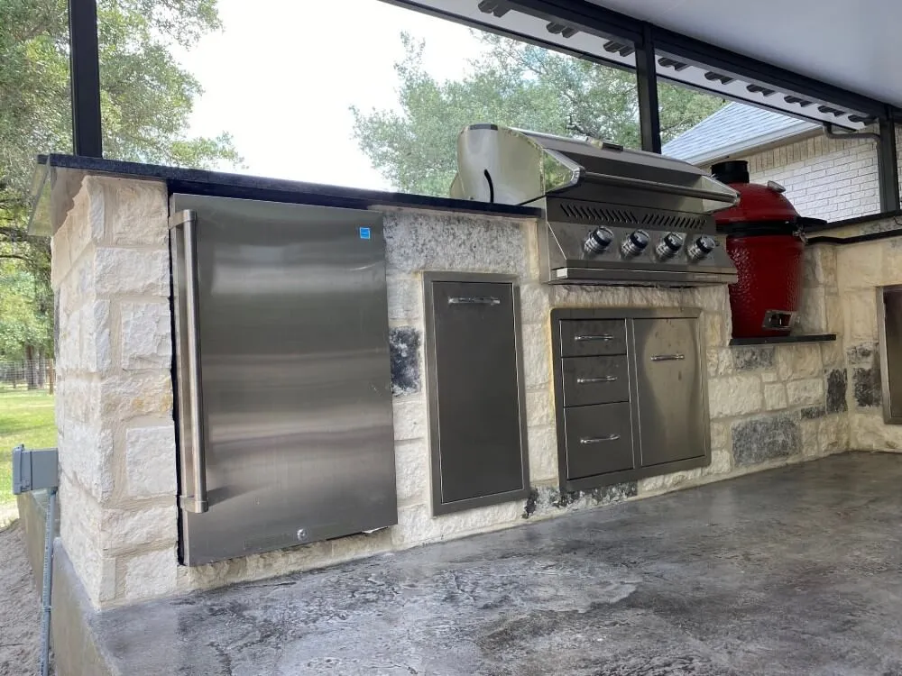 Outdoor kitchen with stone base, stainless steel fridge, grill, and cabinets. San Antonio.