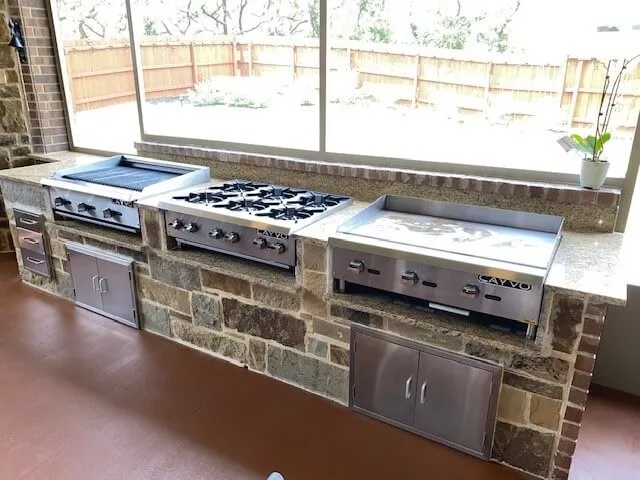 Outdoor kitchen with grills and stovetop, stone countertops.