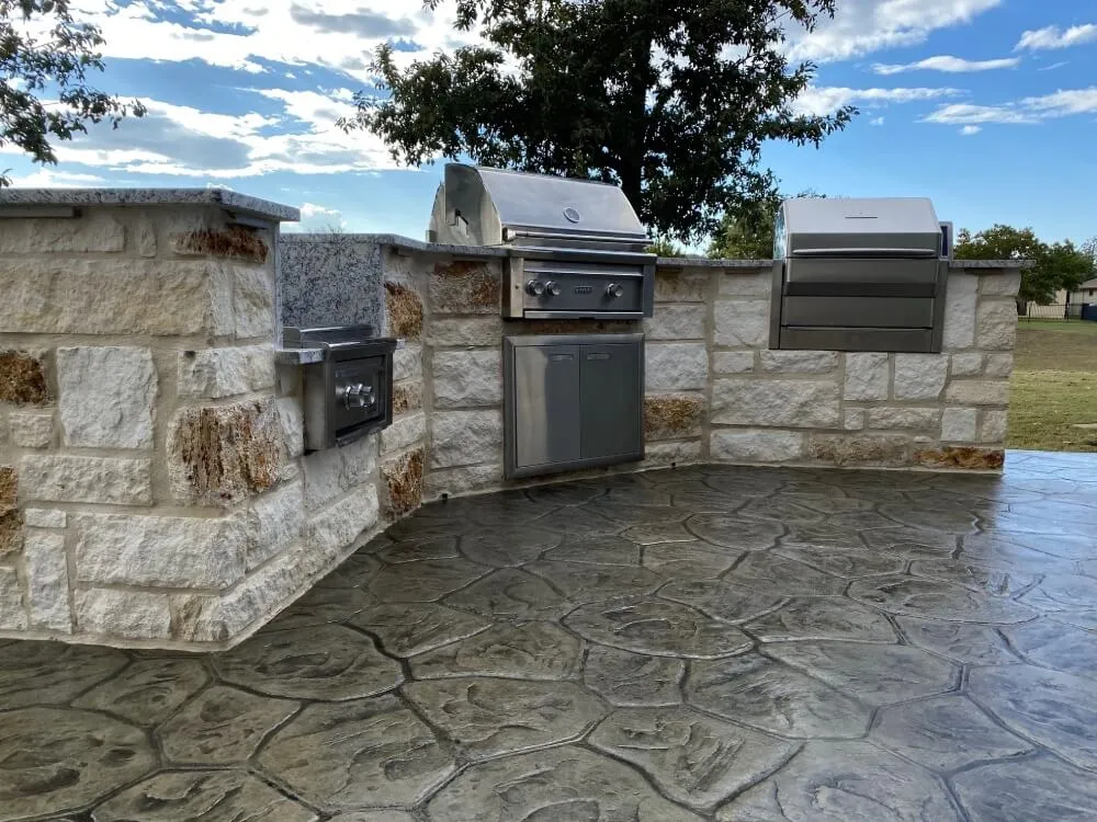 Outdoor kitchen with grills and stone countertop.