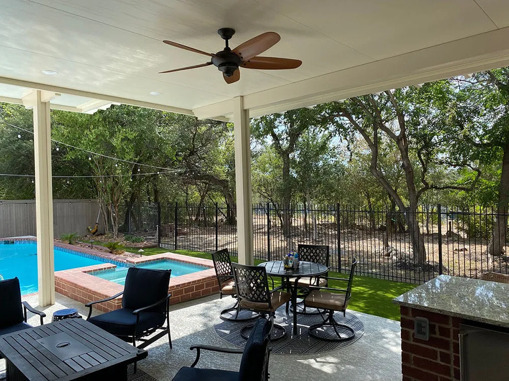 Covered patio with table, pool, and spa in a backyard.