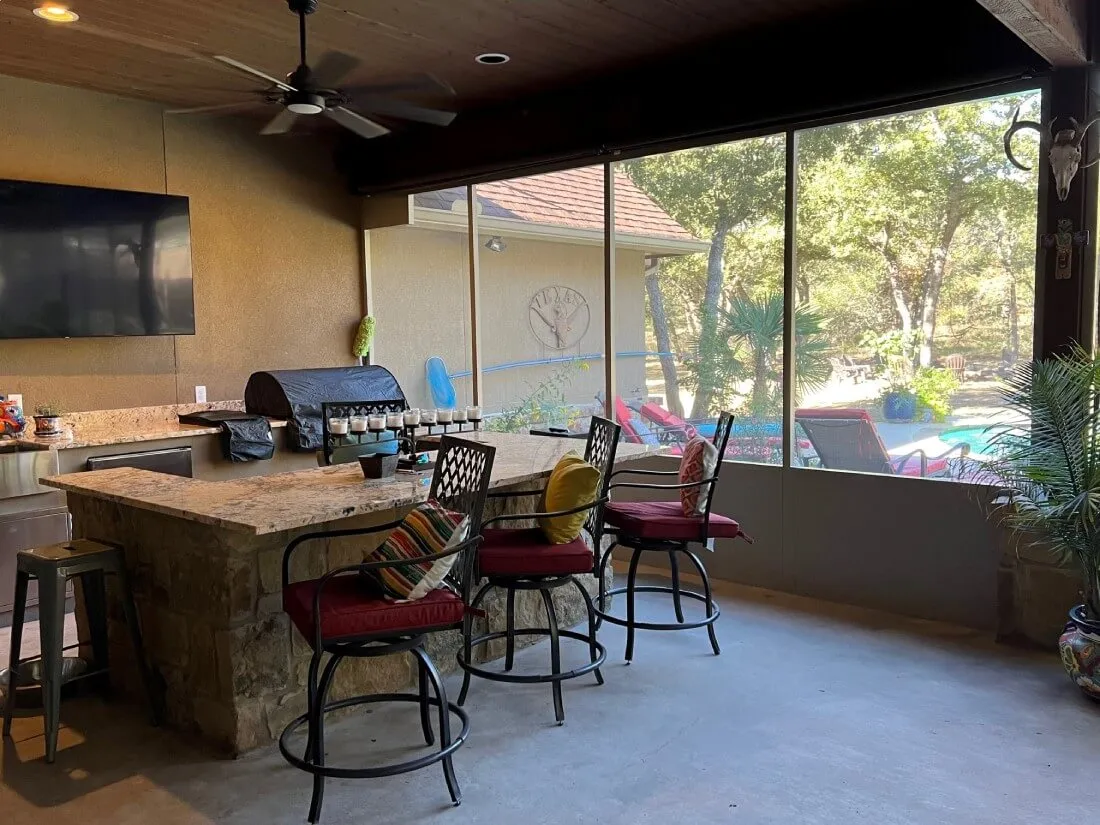 Outdoor kitchen with bar stools in San Antonio patio enclosure.