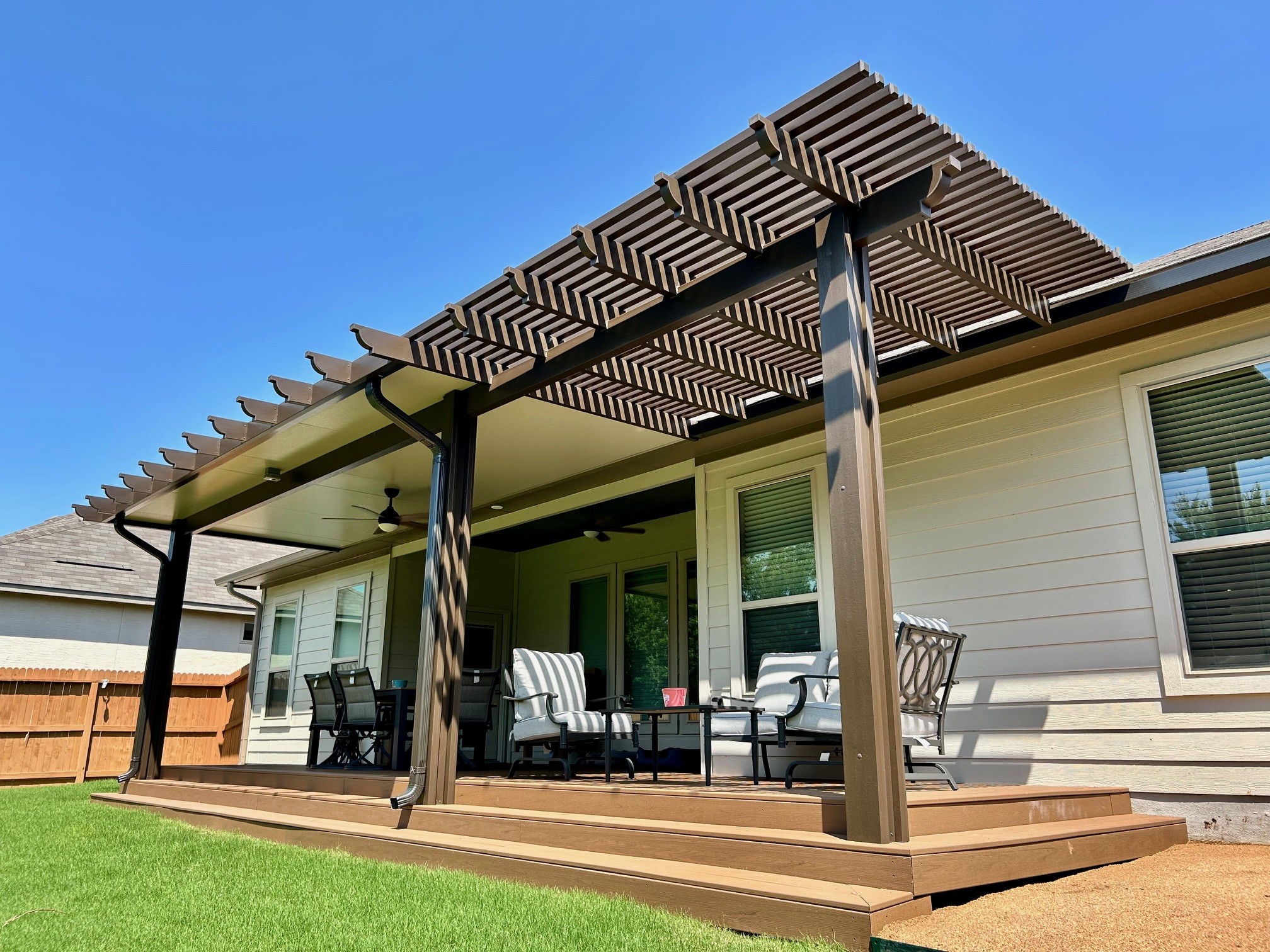 Wooden patio cover with pergola over a backyard patio with outdoor furniture, sunny day, clear blue sky.